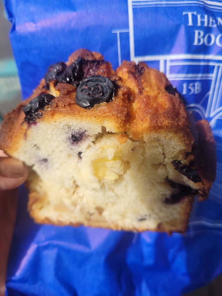 A blueberry muffin held in a blue paper bag, cropped tight on the muffin so no lettering shows