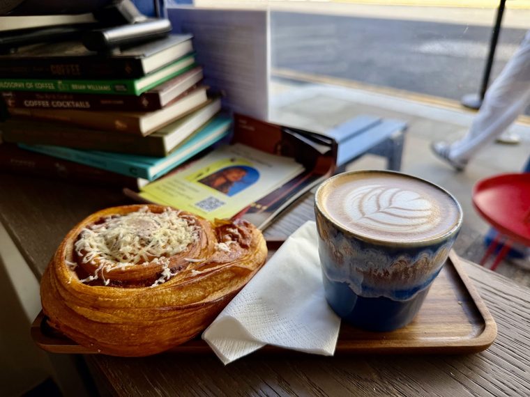 A cruffin-style pastry beside a latte on the window counter
